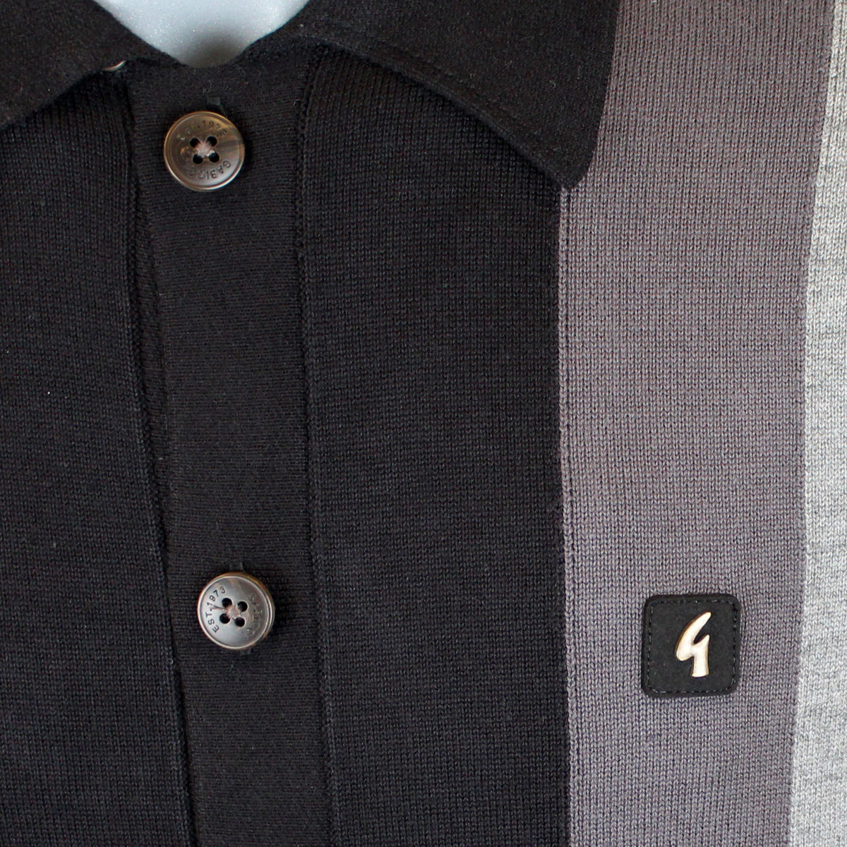 Close-up of a knit polo shirt with a black collar and button placket, a vertical dark gray stripe, and a small black square patch with a white stylized '4' on the chest.