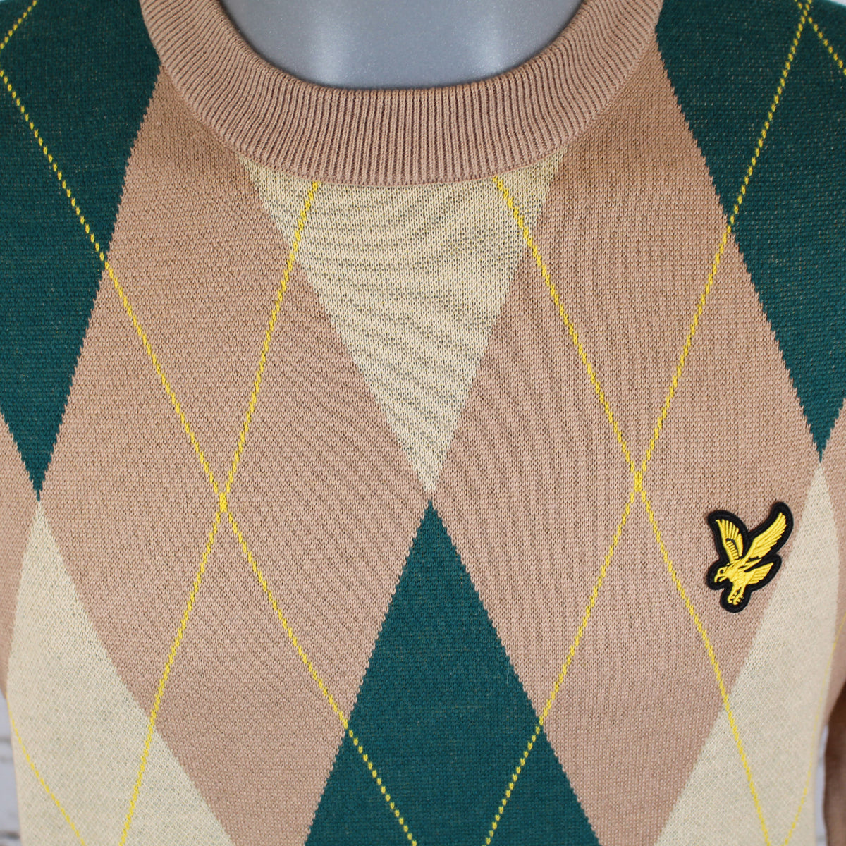 A close-up of a Lyle & Scott's argyle crew neck sweater on a mannequin, featuring a pattern of beige, cream, and dark green diamonds with thin yellow lines, and the signature yellow eagle logo on the chest.