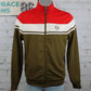 A vintage-style zip-up track jacket displayed on a mannequin torso against a white brick wall. The jacket features a red yoke, a white stripe with olive green double lines across the chest, and an olive green body and sleeves.
