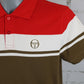 A close-up of a color-blocked short-sleeve polo shirt on a mannequin. The shirt features a bright red upper chest and collar, a wide white middle band, and an olive brown lower body with a thin white stripe.